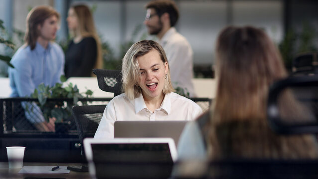 A woman is sitting at a desk with a laptop and smiling
