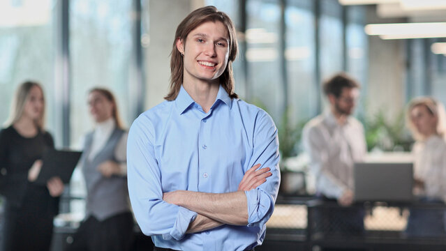 A man with long hair is smiling and standing in front of a group of people