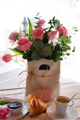 Flower decoration for a mother's day breakfast. Pink heart, roses, tulips, and ranunculus arranged in a white vase. Vertical lifestyle background.