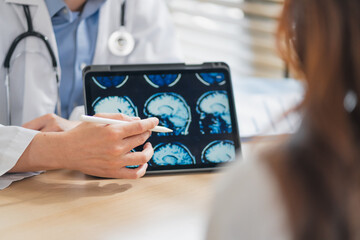 Doctor explaining brain skull MRI scan on tablet to patient during consultation at clinic highlighting neurology diagnosis medical discussion healthcare technology imaging concept professional care. © whyframeshot