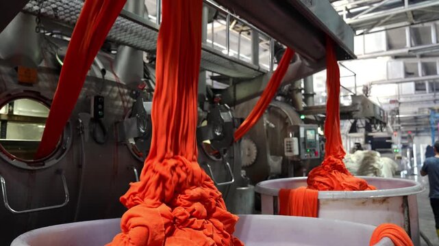 Bright orange fabric flowing from large dyeing machines in a textile factory. Professional industrial footage reflecting technical process, production control and large scale manufacturing.