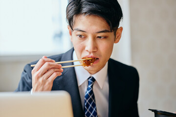 Asian businessman eating meal while working on laptop