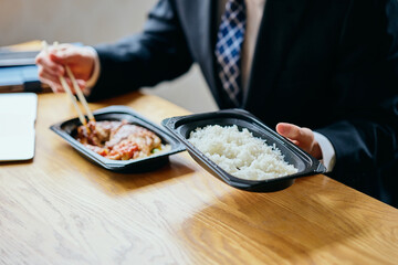 Asian businessman eating bento at desk while working on laptop (close up)	