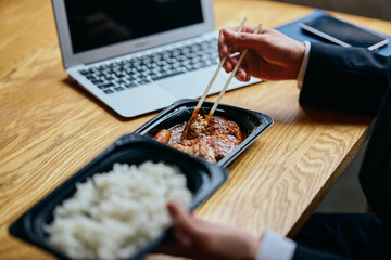 Asian businessman eating bento at desk while working on laptop (close up)	