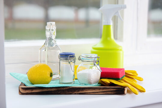 Natural organic eco friendly home cleaning ingredients, white vinegar, lemon, baking soda, citric acid on wood tray on window sill, window on background. Home spring cleaning concept.