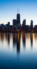Obraz premium Cityscape view at dusk reflecting on water, showing tall buildings with lighted windows, representing urban development, progress, and serenity