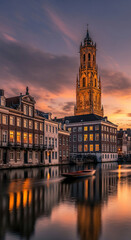 Fototapeta premium Scenic view of old building with high tower, along water at dusk. Reflection of building and sunset sky visible in water, creating calm, tranquil mood