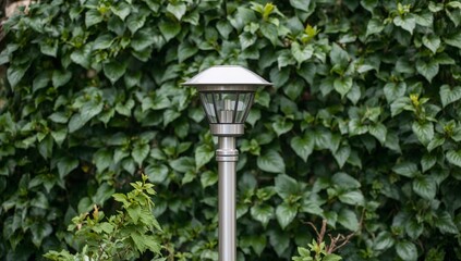 A silver metal lamp post base stands in a garden with lush green leaves