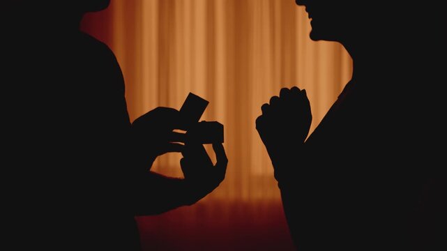 dark black silhouette man proposes to woman holding box with engagement ring gift in hand Adult girl surprised says yes agrees to marry. love emotion. marriage proposal happy couple. wedding concept.