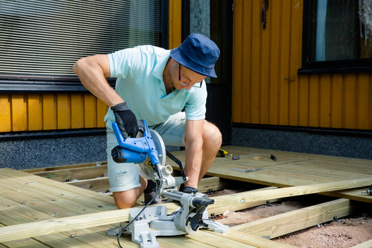 Professional carpenter cutting deck planks with a miter saw during outdoor construction, showing skilled craftsmanship, precise home renovation work.