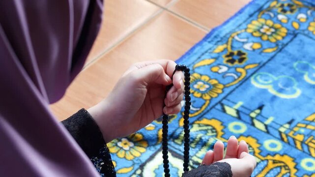 Close up of Muslim woman holding prayer beads while making dua at home. Spiritual worship moment with tasbih in hands, faith and devotion concept.