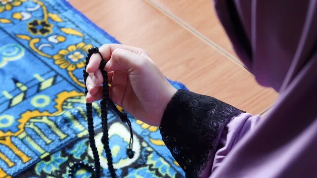 Close up of Muslim woman holding prayer beads while making dua at home. Spiritual worship moment with tasbih in hands, faith and devotion concept.