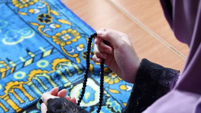 Close up of Muslim woman holding prayer beads while making dua at home. Spiritual worship moment with tasbih in hands, faith and devotion concept.