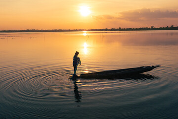 Fototapeta premium Silhouette of fisherman throwing fishing net during sunrise at lake, Asian Thailand