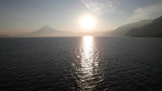 Peaceful lake with mountains, sun rippling on the waves, warm 4K aerial.