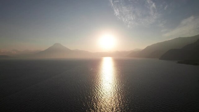 Sunset between volcanoes on serene tropical lake, 4K aerial nature shot, Lake Atitlan, Guatemala.