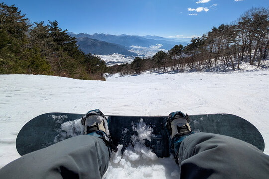 First person view of snowboarder resting on snowy slope overlooking mountain valley