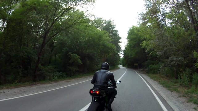 Motorcyclist races motorcycle on woodland country road. Man in helmet rides on sport motorbike at rural road near forest. Guy driving bike during trip. Concept of freedom and adventure. Aerial shot