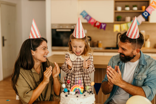 Little girl celebrating birthday with cake and cheerful adults