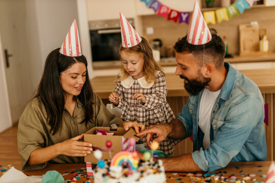 Parents opening present with daughter wearing celebration hats