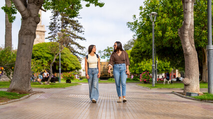 Fototapeta premium Two young women enjoying a casual stroll and conversation in a city park