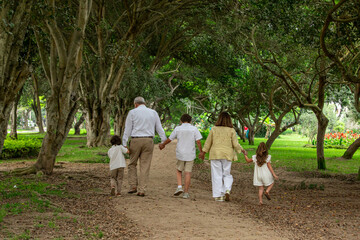 Happy family walking in the park on a sunny day, back view