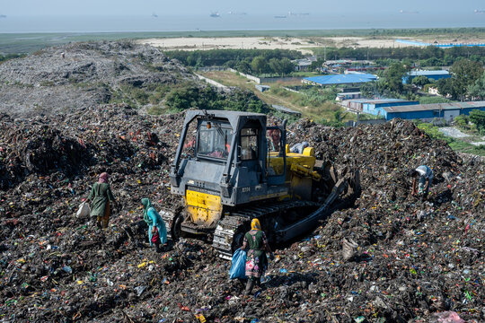 Chattogram, Bangladesh - 25 November 2025: View of a bulldozer amidst the overwhelming expanse of waste at the landfill, where laborers work tirelessly under the open sky.