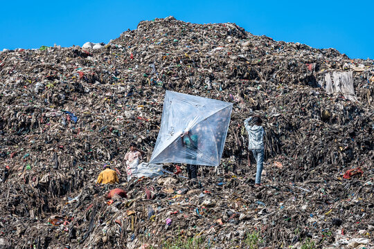 Chattogram, Bangladesh - 26 November 2025: View of a sprawling landscape of refuse, where workers sift through the debris under a makeshift shelter, contrasting against the clear sky.