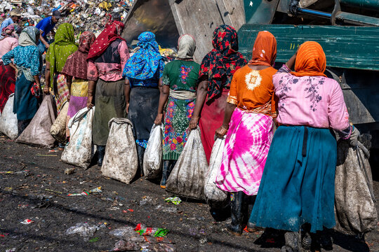 Chattogram, Bangladesh - 26 November 2025: View of women carrying heavy sacks across a vibrant, textured landscape of discarded materials, a tableau of resilience against a backdrop of refuse.