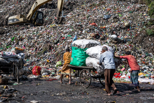Chattogram, Bangladesh - 26 November 2025: View of workers pushing carts through a sprawling landfill under the watchful eye of a towering excavator.