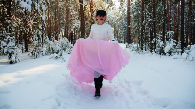 A woman in a snowy forest wearing a stylish white top and a flowing pink skirt, joyfully spinning in the winter landscape, capturing a magical moment in nature.