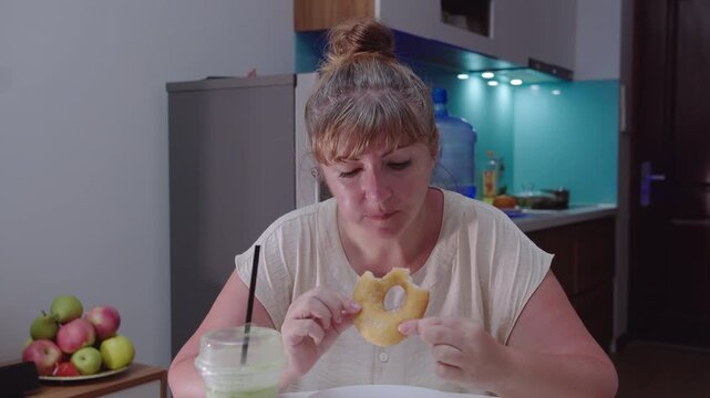 Woman eats a curd ring, sitting at a table, against the background of the kitchen