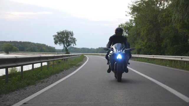 Young man travelling on a motorbike. Biker ride at dam road near lake or river. Motorcyclist driving his motorcycle on country route during journey. Concept of freedom and adventure at trip. Close up