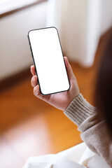 Obraz premium Vertical mockup image of a woman holding and using mobile phone with blank desktop screen at home