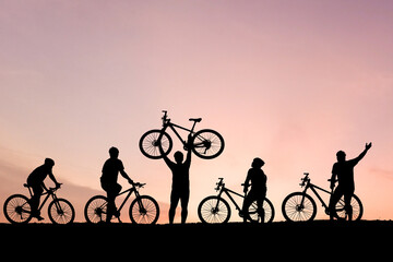 Silhouetted figures enjoying a bike ride during a sunset, highlighting the beauty of outdoor activity and freedom. A person is holding a bicycle
