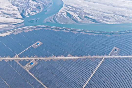 Aerial view of a vast solar panel farm sprawling beneath the winding, icy river, a stark contrast of human engineering and nature's artistry, Gaibandha, Rangpur Division, Bangladesh.