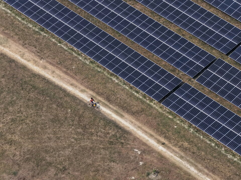 Aerial view of a cyclist riding along a dirt path, juxtaposed against rows of dark solar panels, creating a striking contrast of nature and technology, Gaibandha, Rangpur Division, Bangladesh.