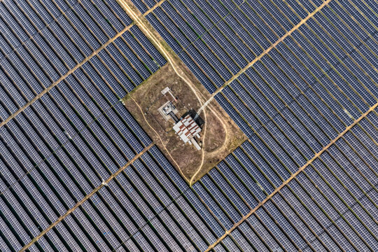 Aerial view of solar panels reflecting the sky's hue, juxtaposed with the stark white buildings and parched earth below, Gaibandha, Rangpur Division, Bangladesh.