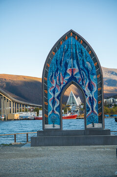 Distinctive blue mosaic art installation frames Tromso waterfront views with Arctic Cathedral visible across harbor waters, creating compelling travel and cultural imagery for Norway tourism.