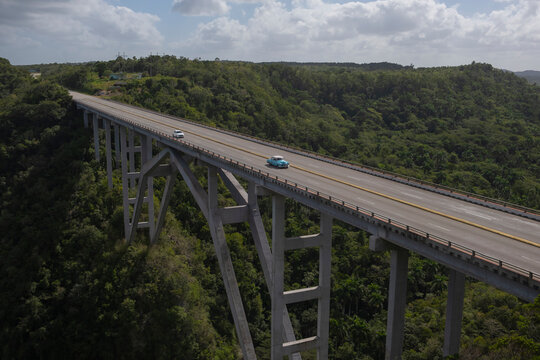 Aerial view of an old American classic car on empty high concrete bridge and highway road trough green tropical forest and mountains over a deep canyon. Bacunayagua Bridge, Matanzas, Cuba.
