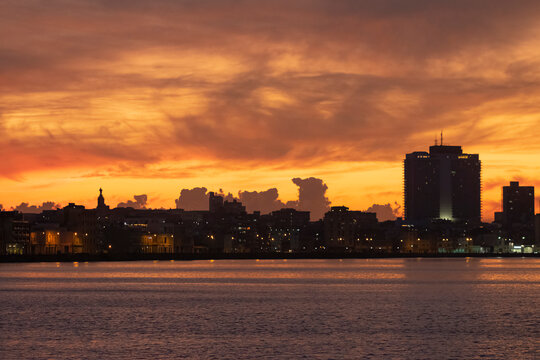 Havana city scape skyline by waterfront Malecon street during sunset time - yellow, orange, red clouds reflecting in the ocean.