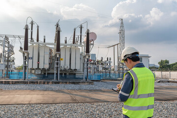 Engineer recording inspection data at power transformer yard in electrical substation, documenting equipment status and asset condition to support preventive maintenance and grid stability. © JD Studio