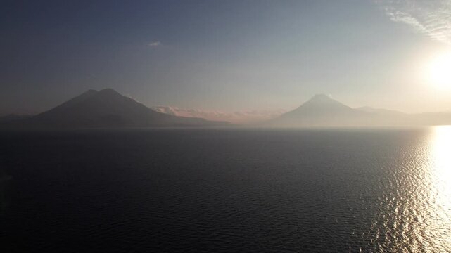 Sun rays over tropical lake, atmospheric aerial background shot, with volcanos in distance. Lake Atitlan, Guatemala, 4K