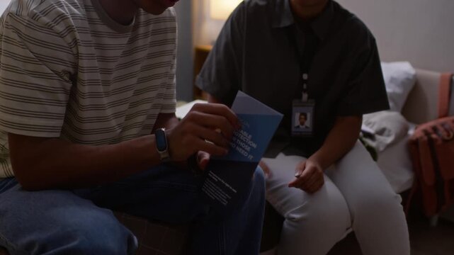 Cropped slowmo shot of unrecognizable Black female social worker giving brochure and talking about social assistance program during home visit to male participant
