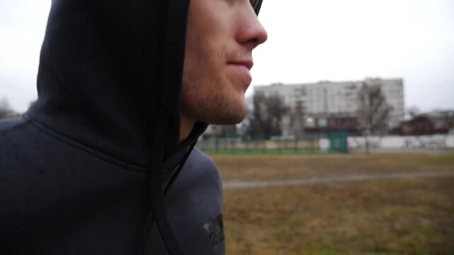 Young sportsman jogging on school stadium at cloudy day. Athletic sporty man running on athletic field. Strong guy in sportswear doing cardio training outdoor. Concept of active healthy lifestyle