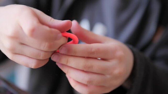 child's hands stretching a neon orange elastic band in slow motion. A tactile sensory study of tension and elasticity as a boy pulls a vibrant rubber cord toward the camera, emphasizing fine motor exp