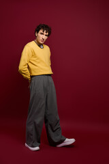 Handsome man showcases stylish outfit against rich maroon backdrop with confidence and flair