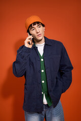 Stylish man in vibrant colors talking on the phone against a bold orange backdrop