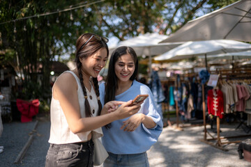 Asian friends shopping and smiling using smartphone at market © Apichat