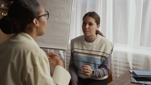 Over shoulder view of unrecognizable tutor gesticulating and explaining pronunciation while teen student listening to her